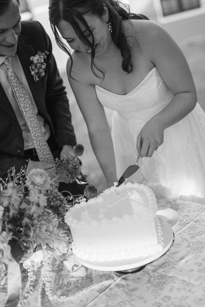 Black and white photo of a bride and groom cutting into their wedding cake
