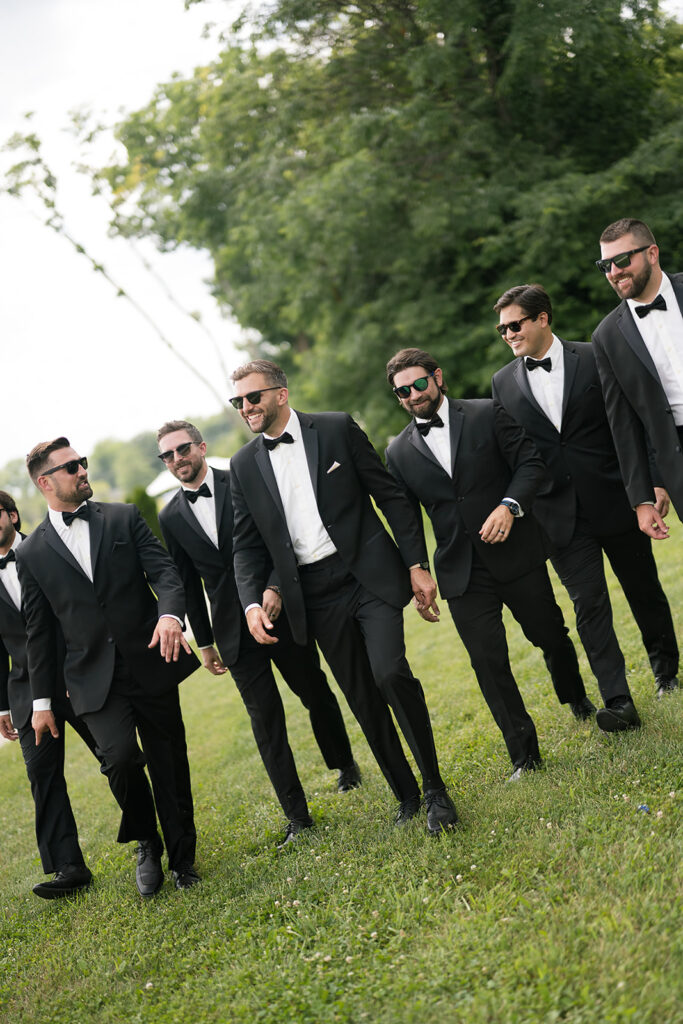 Groomsmen walking in tuxedos and sunglasses laughing together at Daniel’s Vineyard wedding