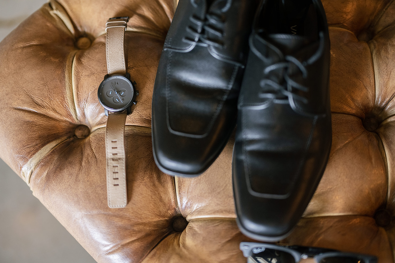 Close up shot of grooms wedding details featuring black shoes, watch, and sunglasses