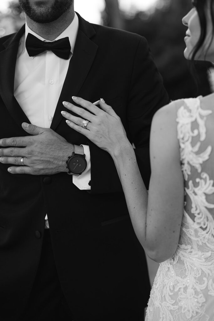 Black and white close-up of bride’s hand resting on groom’s chest, showing her ring.