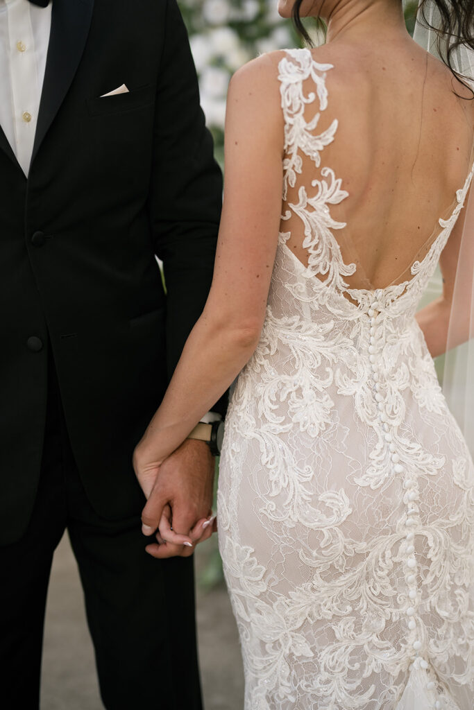 Detail shot of bride and groom holding hands, showing lace detail on the back of her gown.