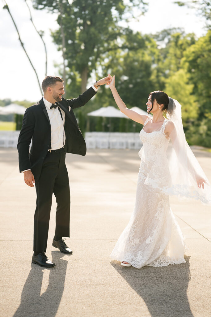 Groom twirling bride outdoors on the Ceremony Pad, sunlight glowing around them.