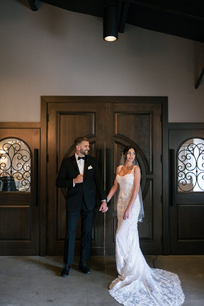 Bride and groom holding hands in front of dark wooden doors inside Daniel’s Vineyard.
