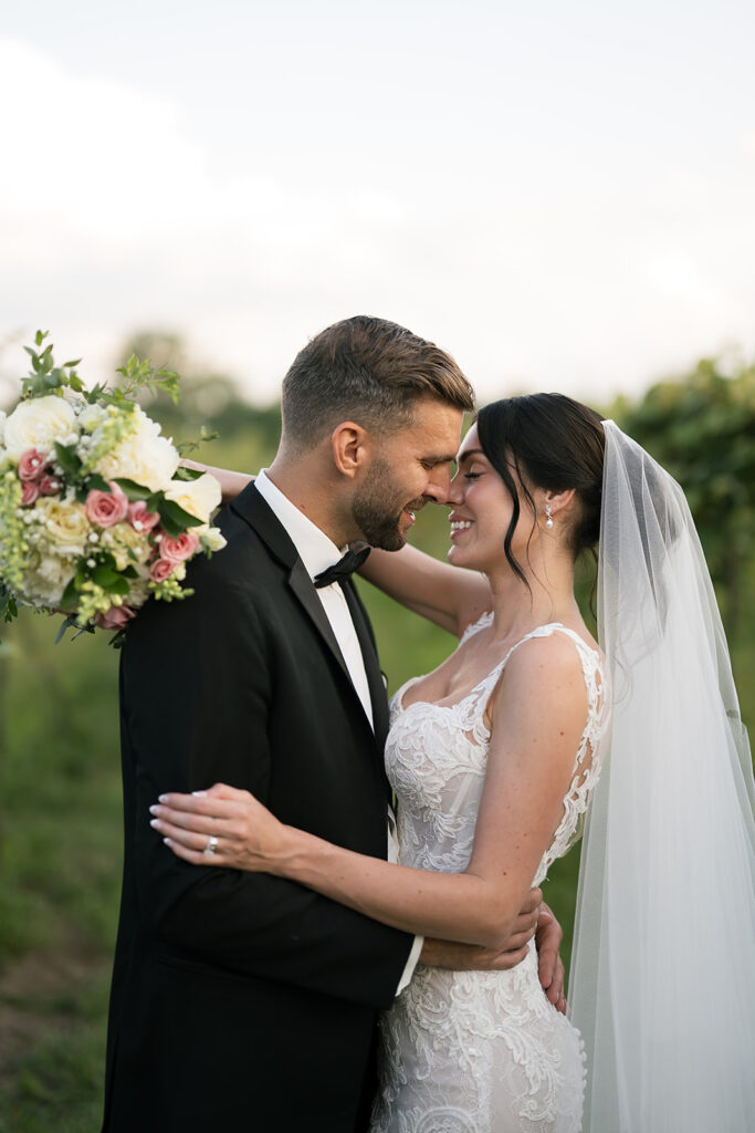 Bride and groom standing close together in the vineyard, foreheads touching as they smile.