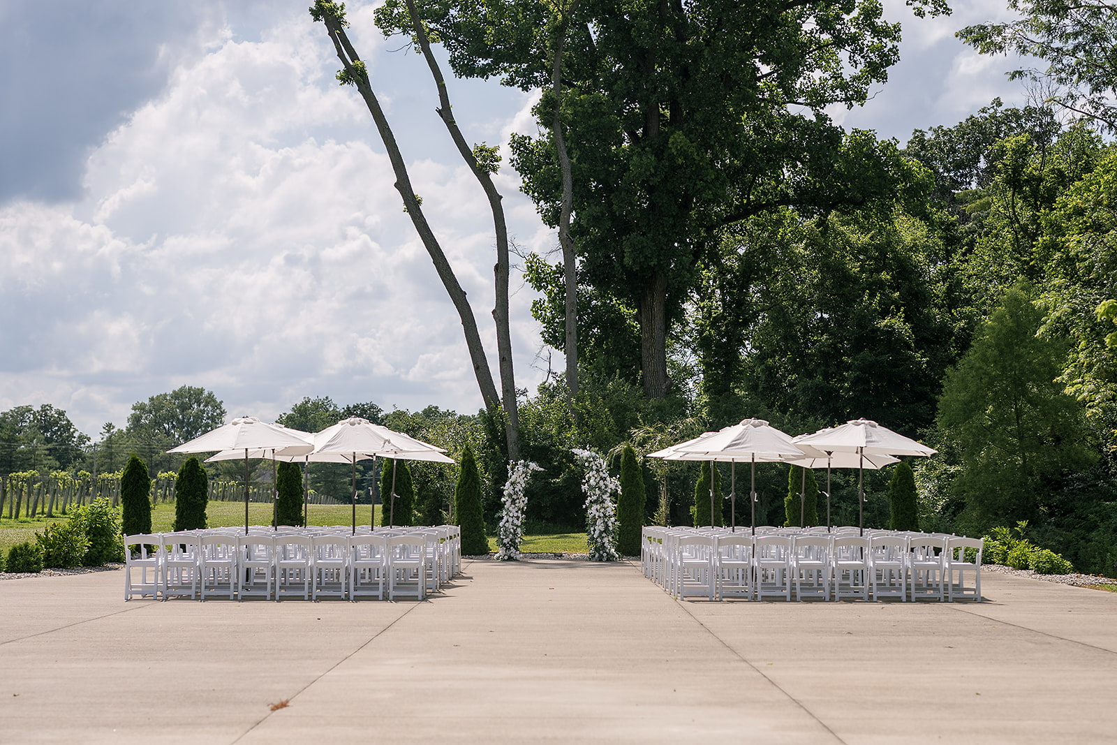 Outdoor Ceremony Pad setup at Daniel’s Vineyard with white chairs, umbrellas, and floral arbor