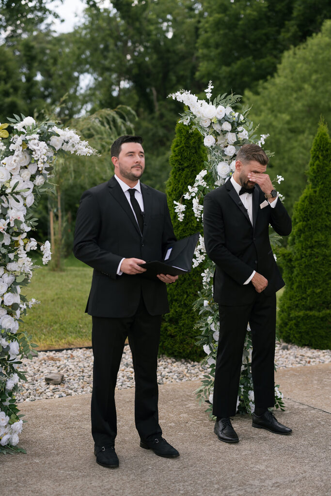 Groom wiping away tears while waiting at altar during outdoor ceremony at Daniel’s Vineyard