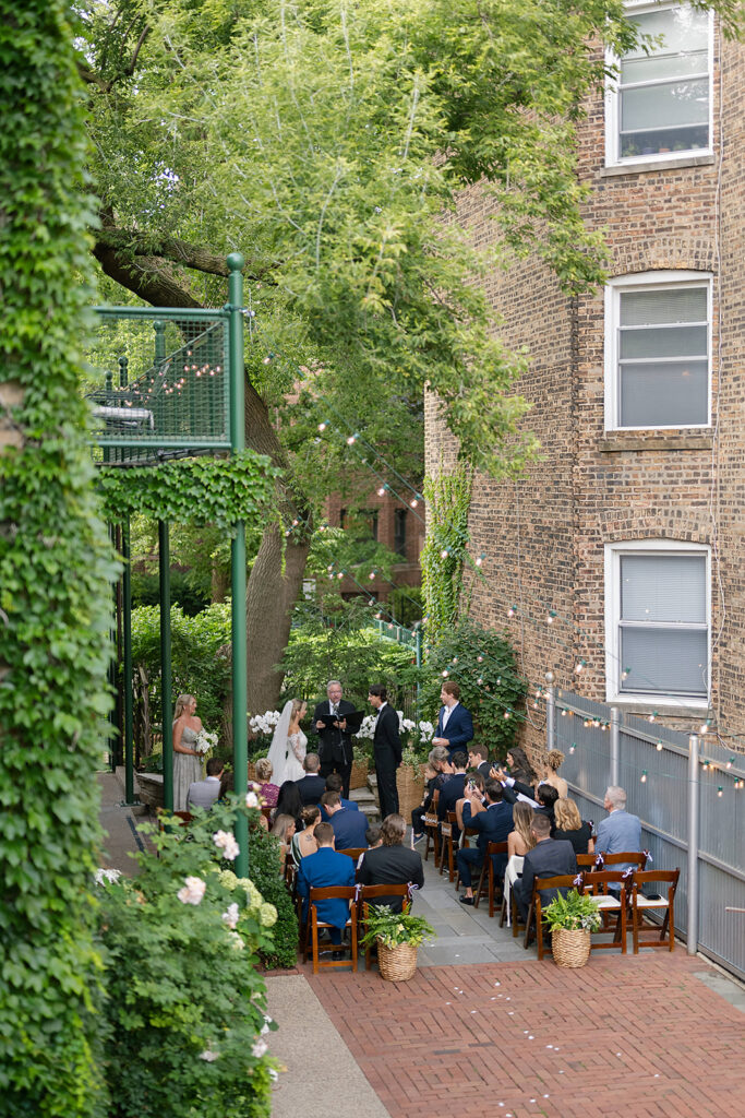 Wide view of outdoor ceremony at Firehouse Chicago with guests seated between ivy-covered walls.