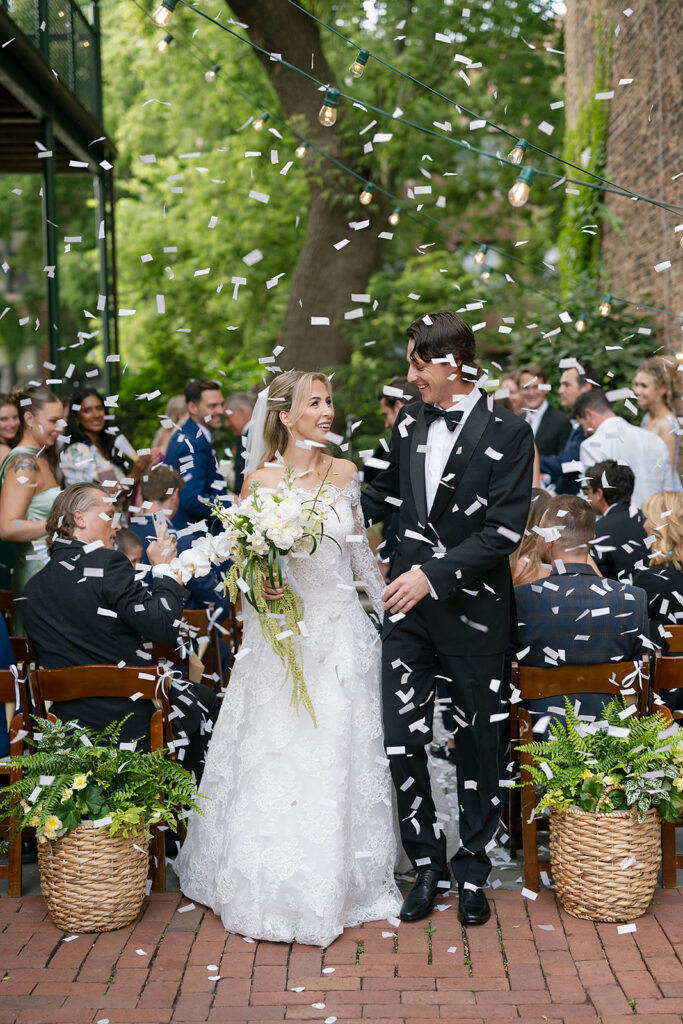 Bride and groom smiling as white confetti fills the air after their Firehouse Chicago micro wedding ceremony.