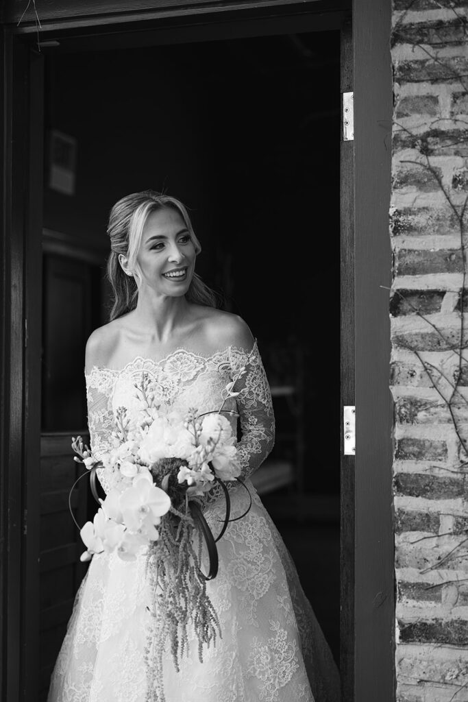Black and white photo of a bride walking out to share a first look with her father