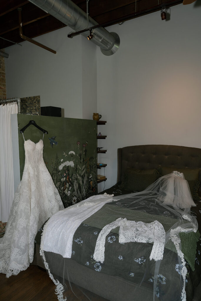 Brides dress hanging with her jacket and veil sprawled out on the bed