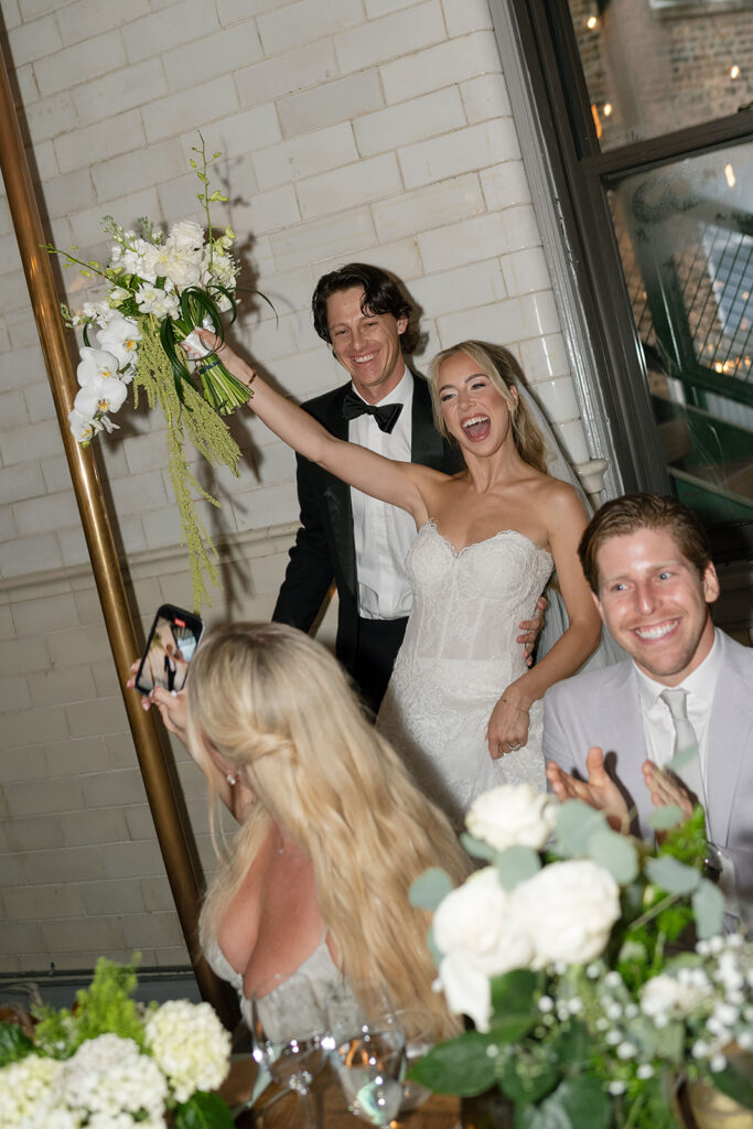 Bride and groom laughing and raising their hands while making their reception entrance.