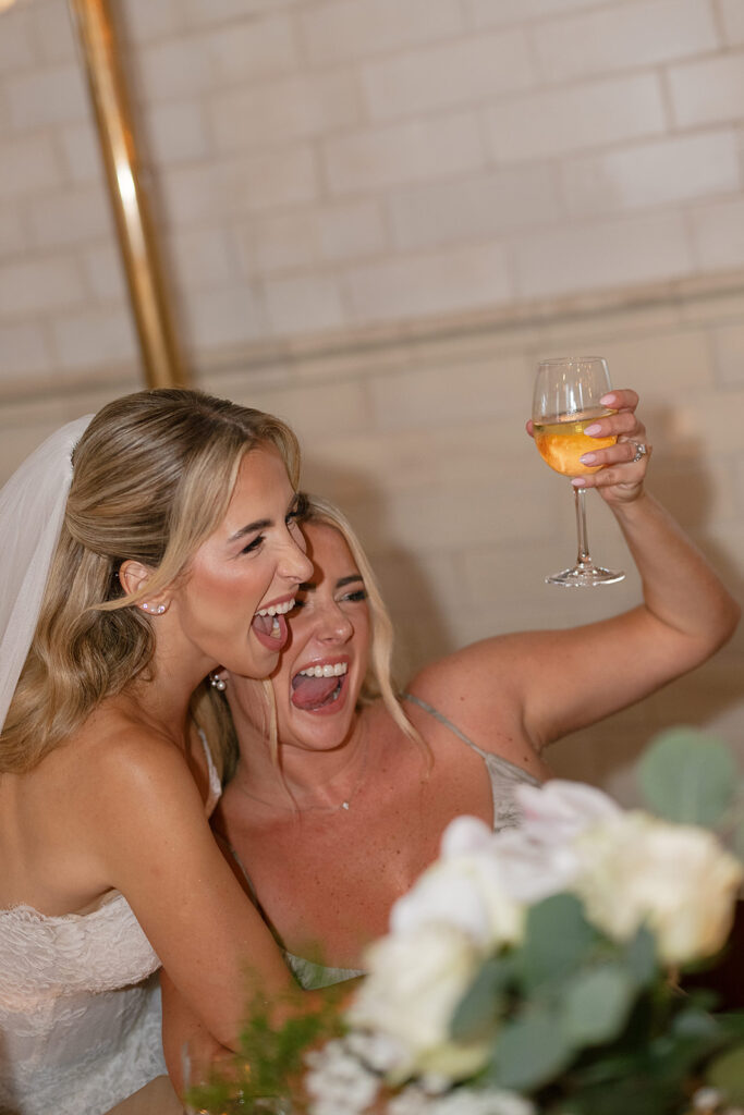 Bride laughing and raising a glass of wine with a guest during the reception.