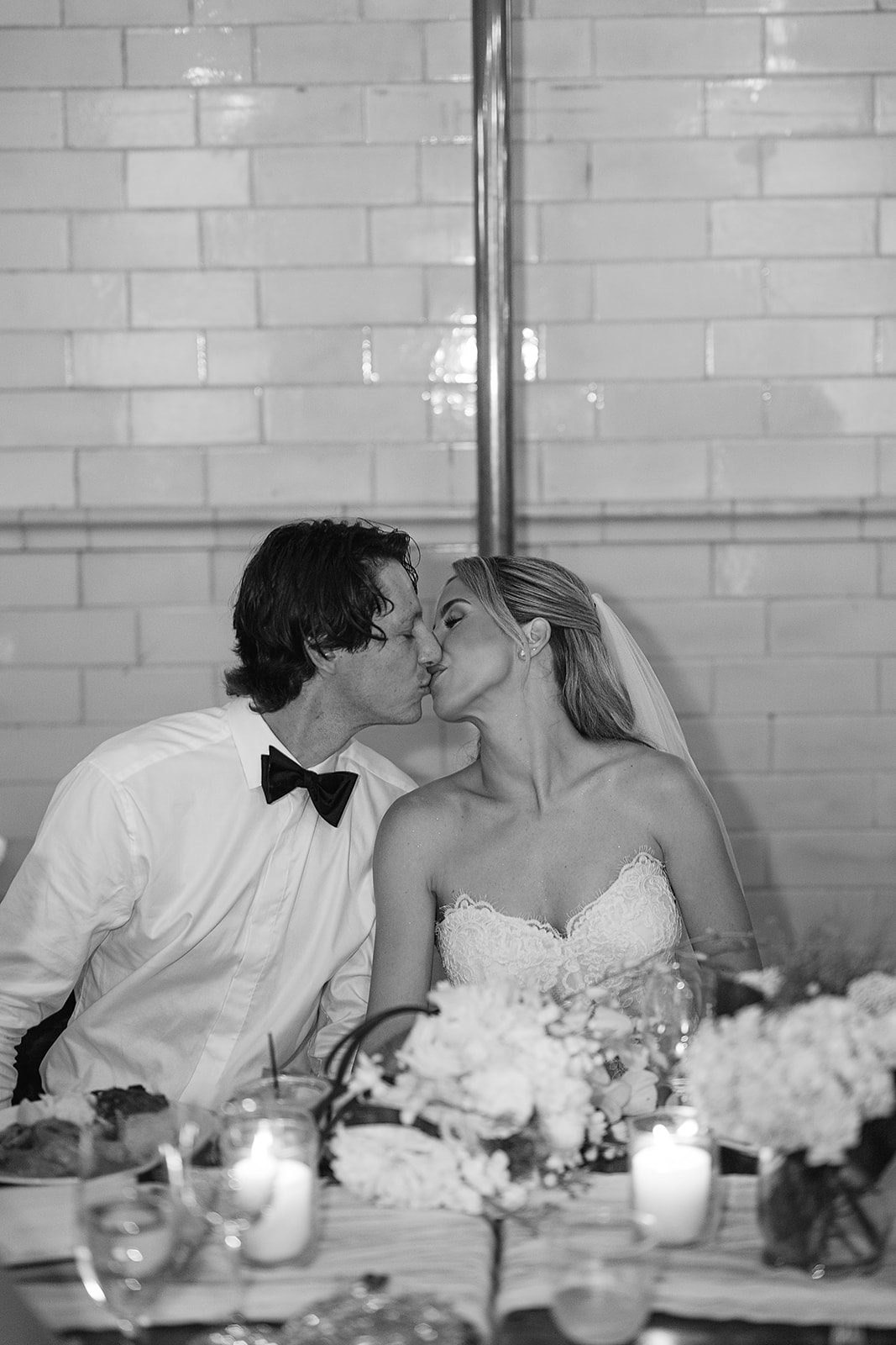 Bride and groom kissing at their sweetheart table, surrounded by florals and candlelight.