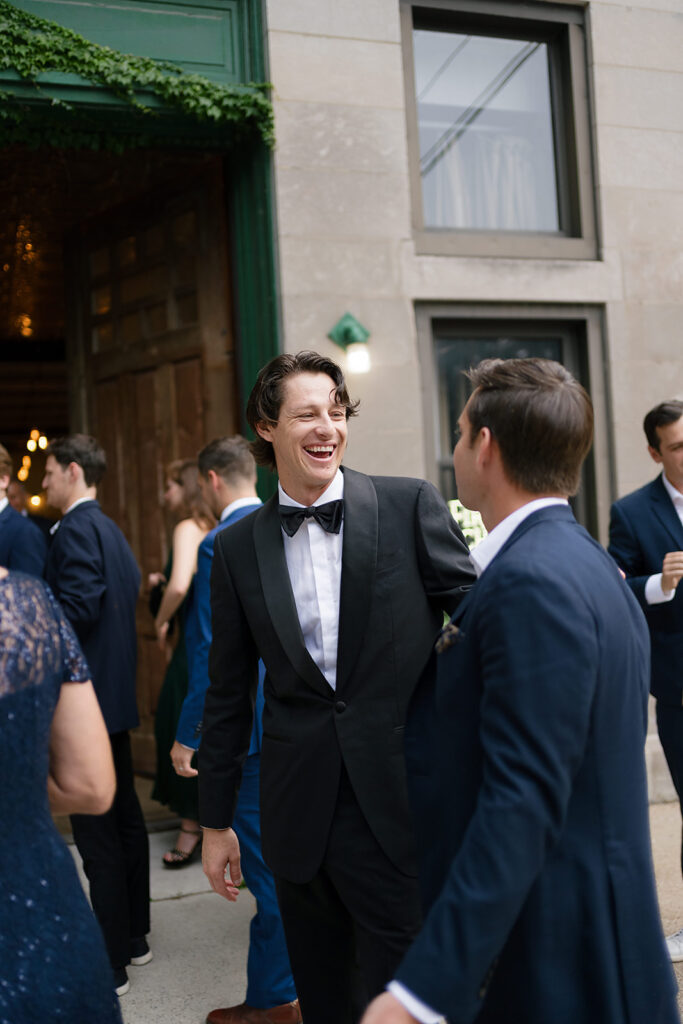 Groom laughing and talking with a guest during wedding party photos.