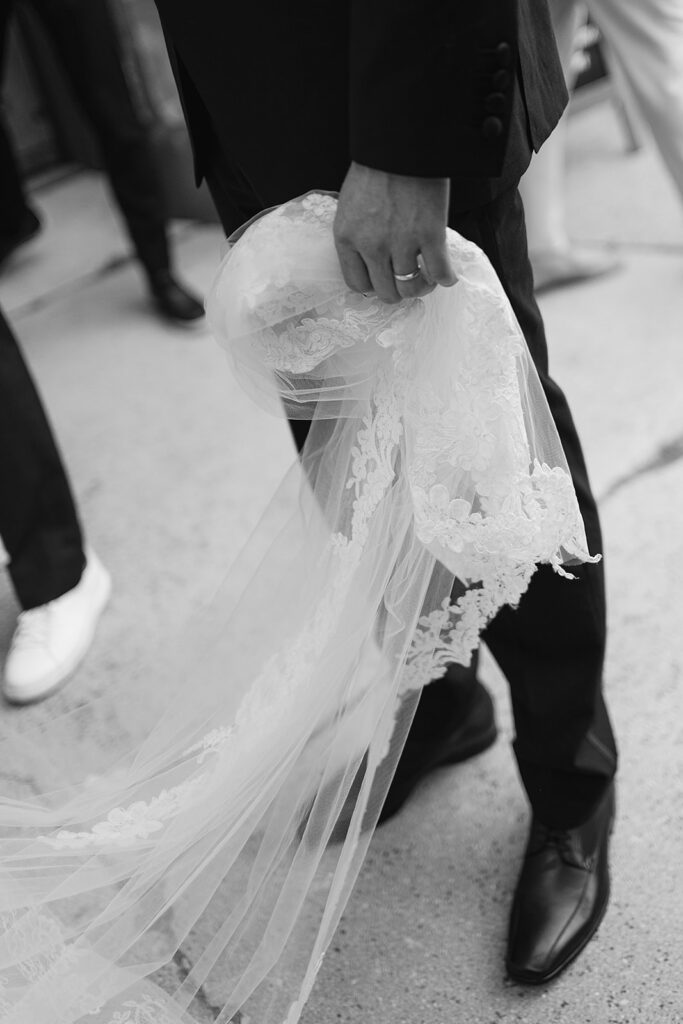 Black and white photo of the groom holding his brides train