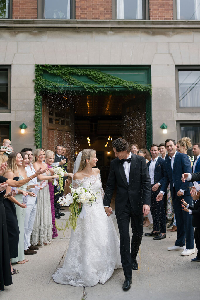 Bride and groom walking through a joyful send-off with guests cheering outside Firehouse Chicago.