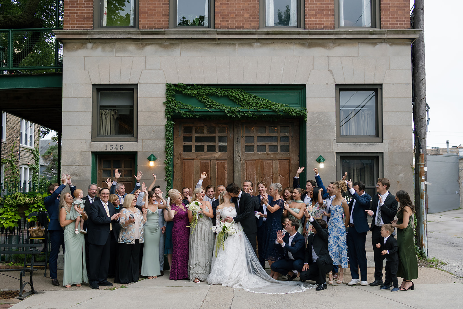 Full wedding group photo outside Firehouse Chicago with brick and ivy backdrop.